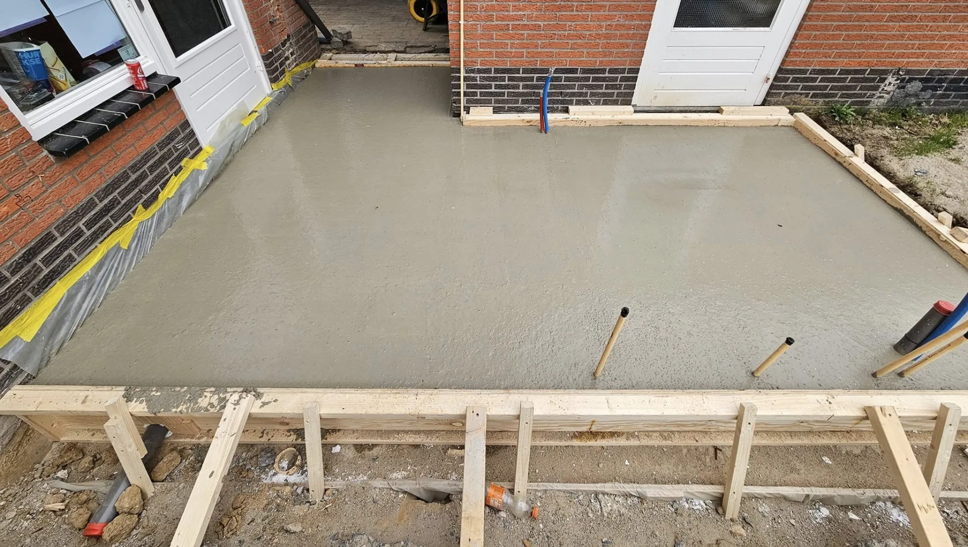 Vers gestorte betonvloer met bekisting en leidingdoorvoeren naast een bestaande woning